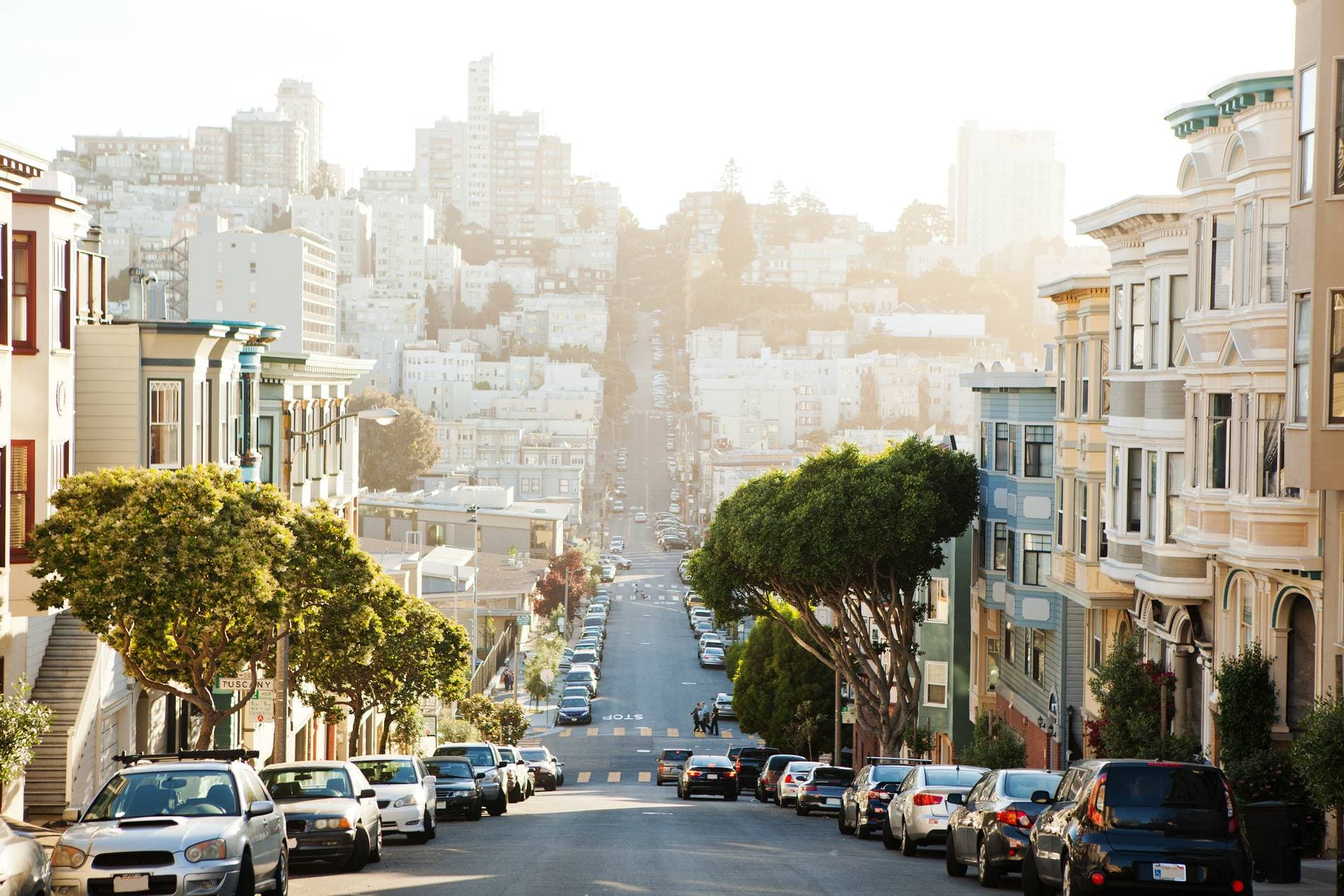 A sunlit San Francisco street of bay-window houses running down toward Russian Hill
