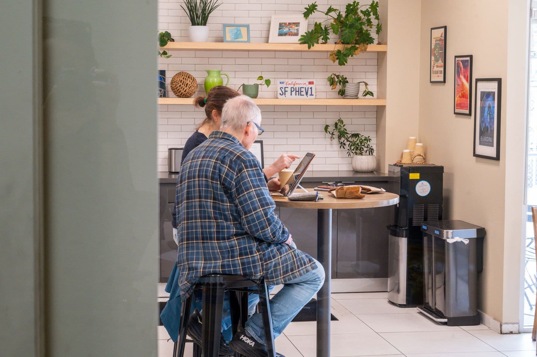 A customer working on a laptop at the lobby's coffee bar, plants on the shelves