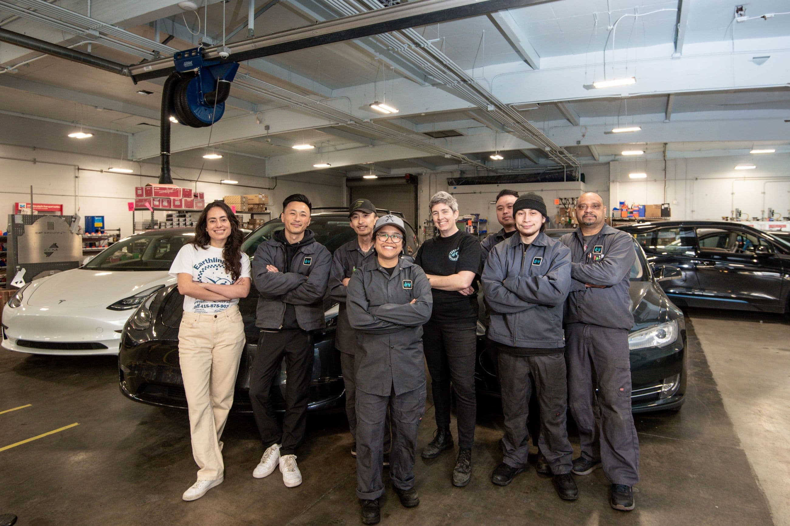 The Earthling crew together in the bays, in front of a white Model 3 and a dark Model S