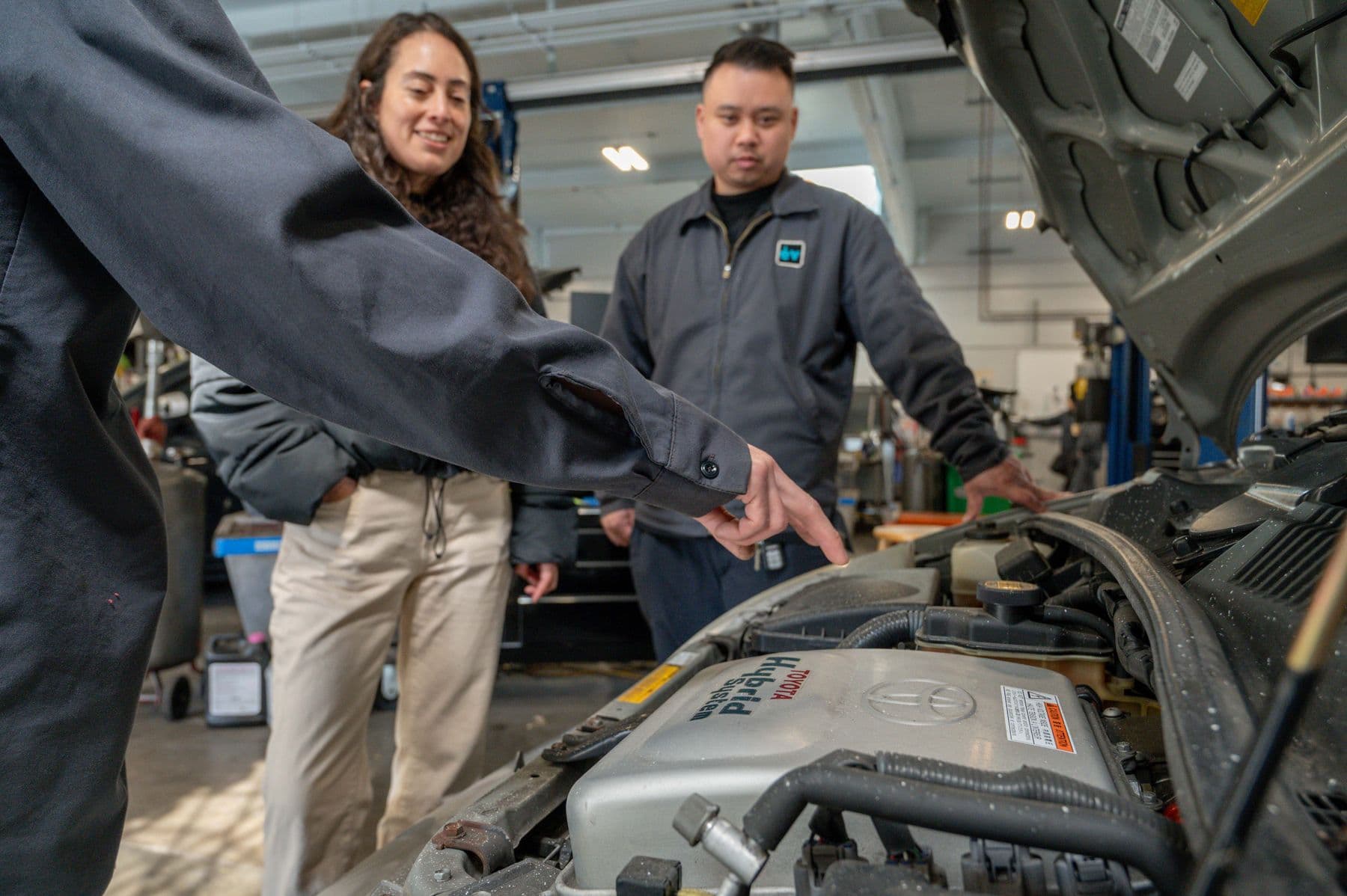 A technician pointing out a part in a hybrid's engine bay while the customer looks on