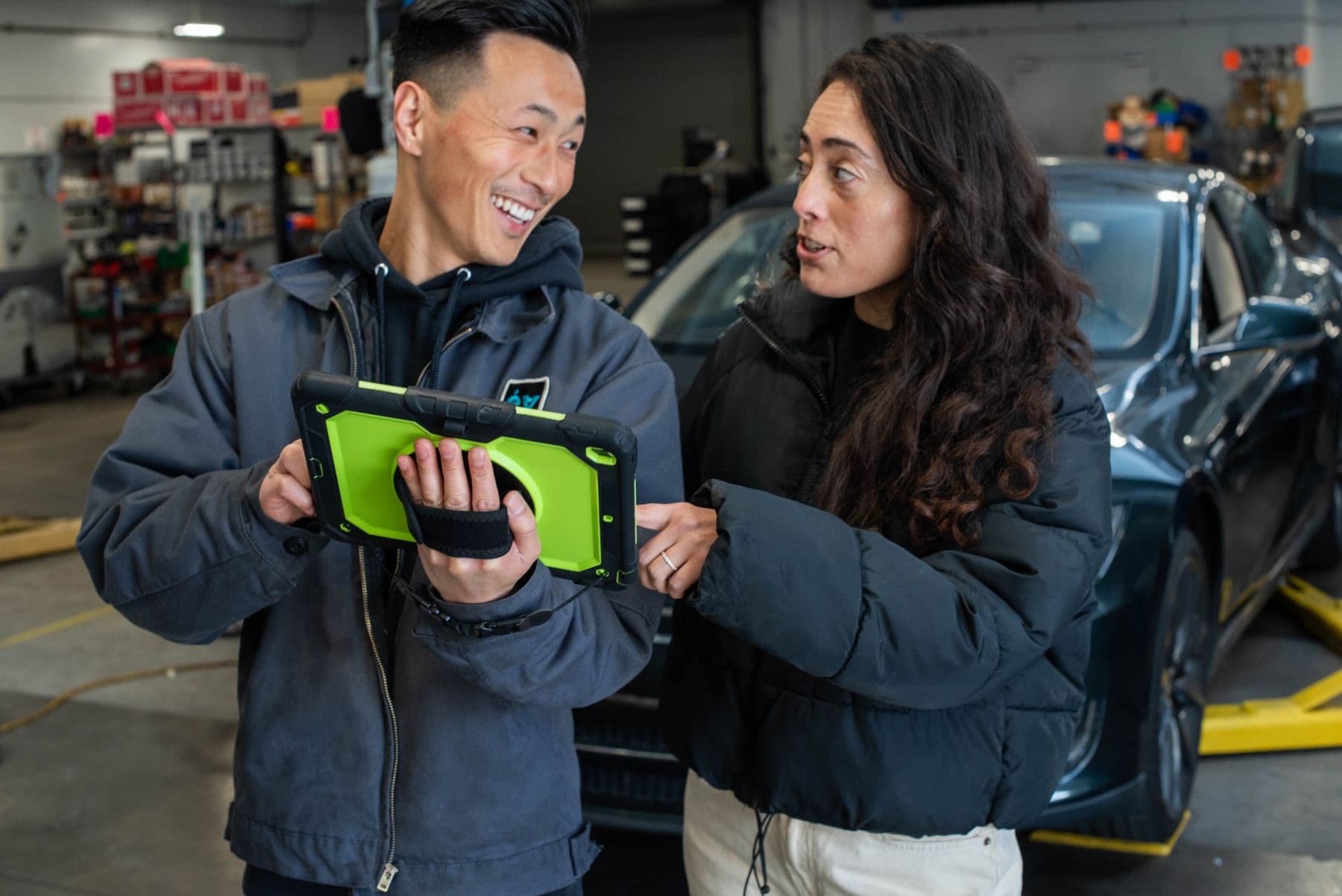 A technician showing a customer the inspection photos on a tablet beside her car