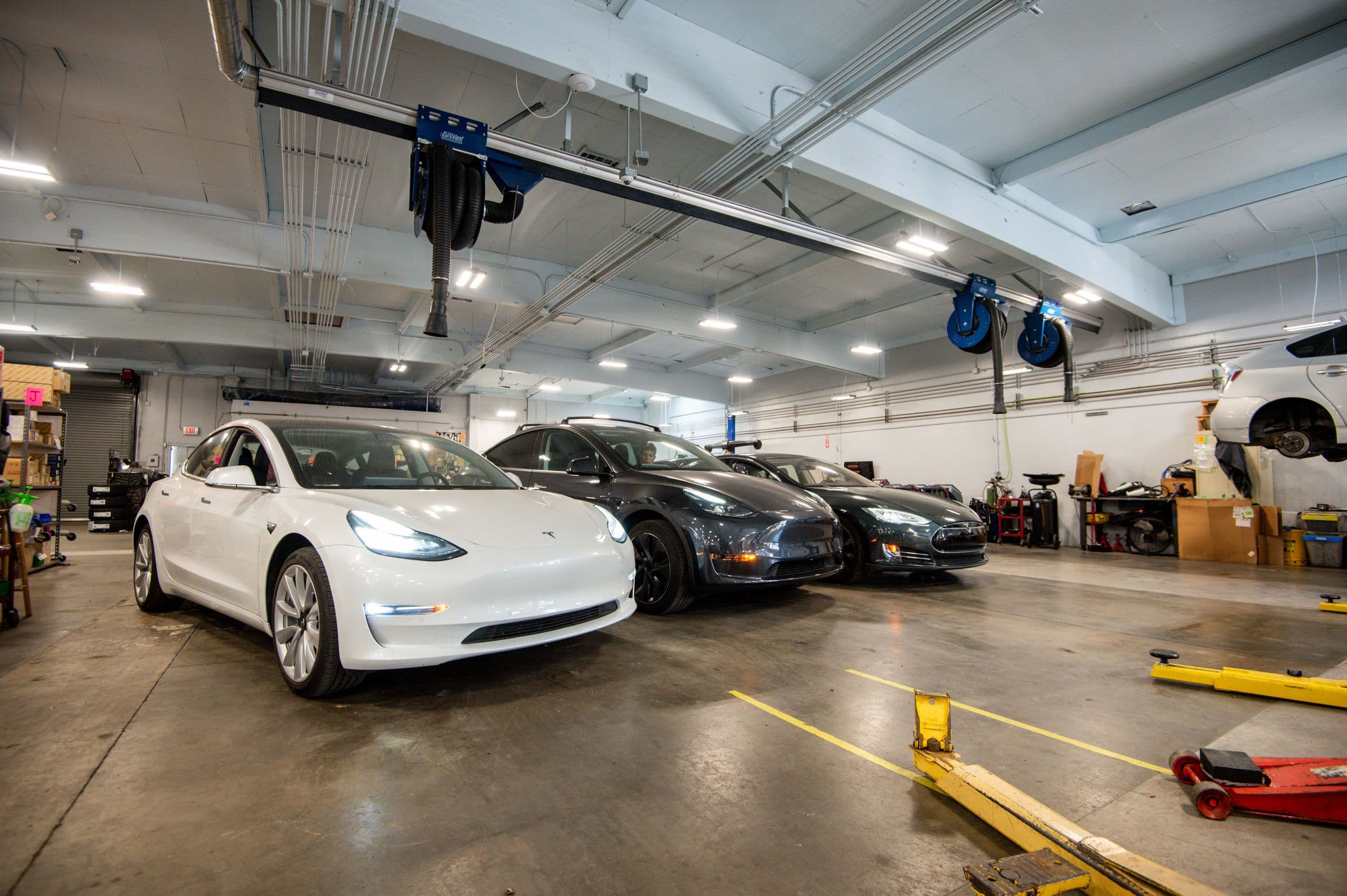 A white Model 3, a gray Model Y and a dark Model S parked side by side in the Earthling bays