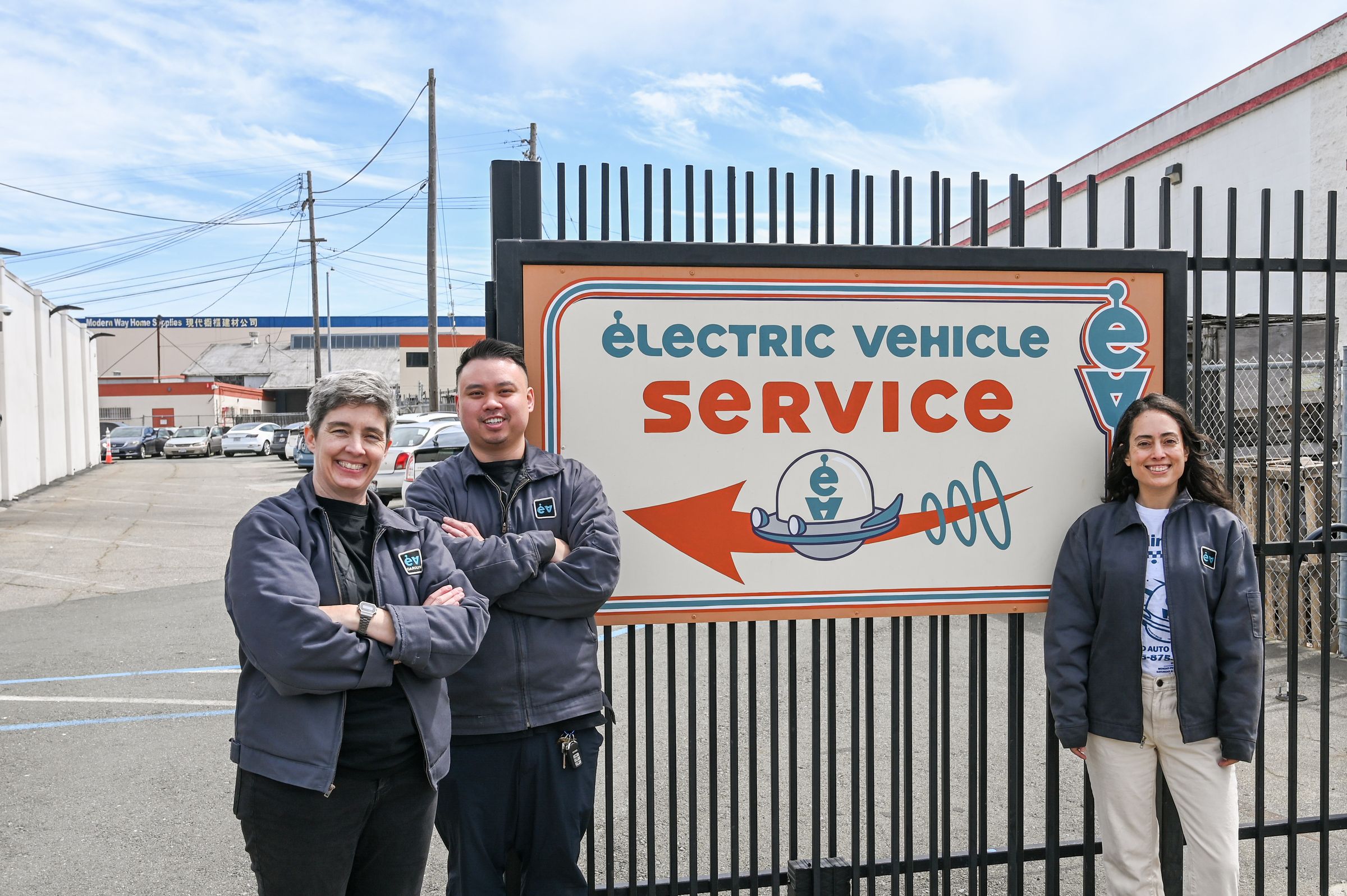 Three of the Earthling team in shop jackets beside the Electric Vehicle Service sign on the front gate