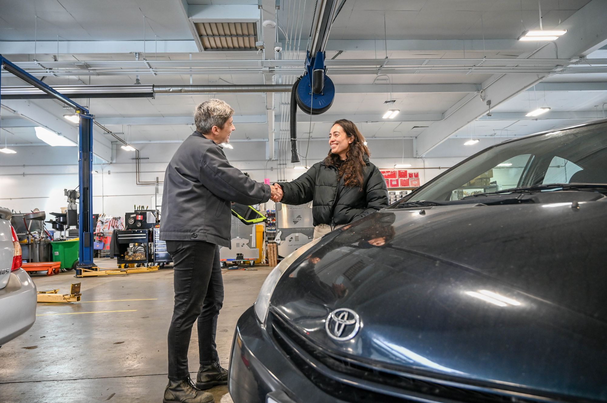 A customer shaking hands with an Earthling service advisor beside her Prius