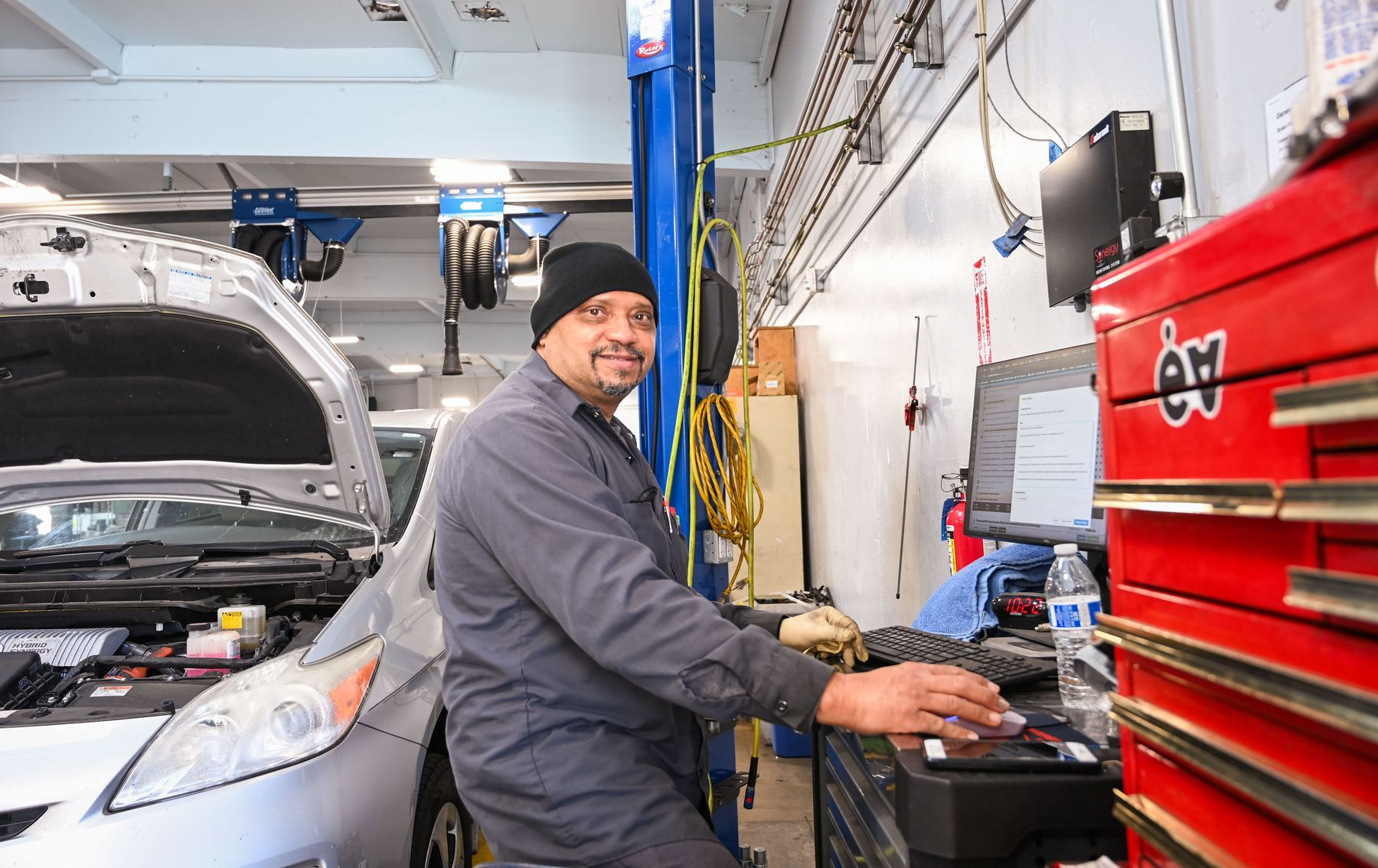 An Earthling technician at his red toolbox and diagnostic screen, a Prius open beside him
