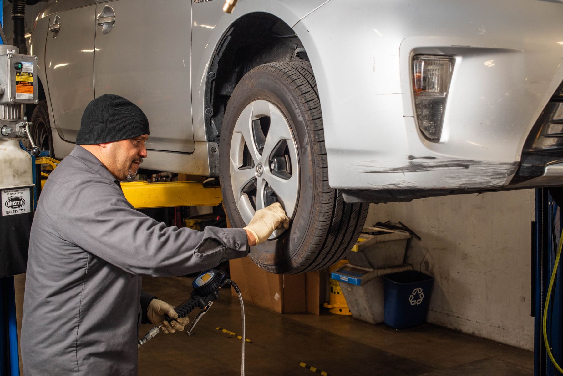A technician tightening a wheel on a Prius raised on the lift