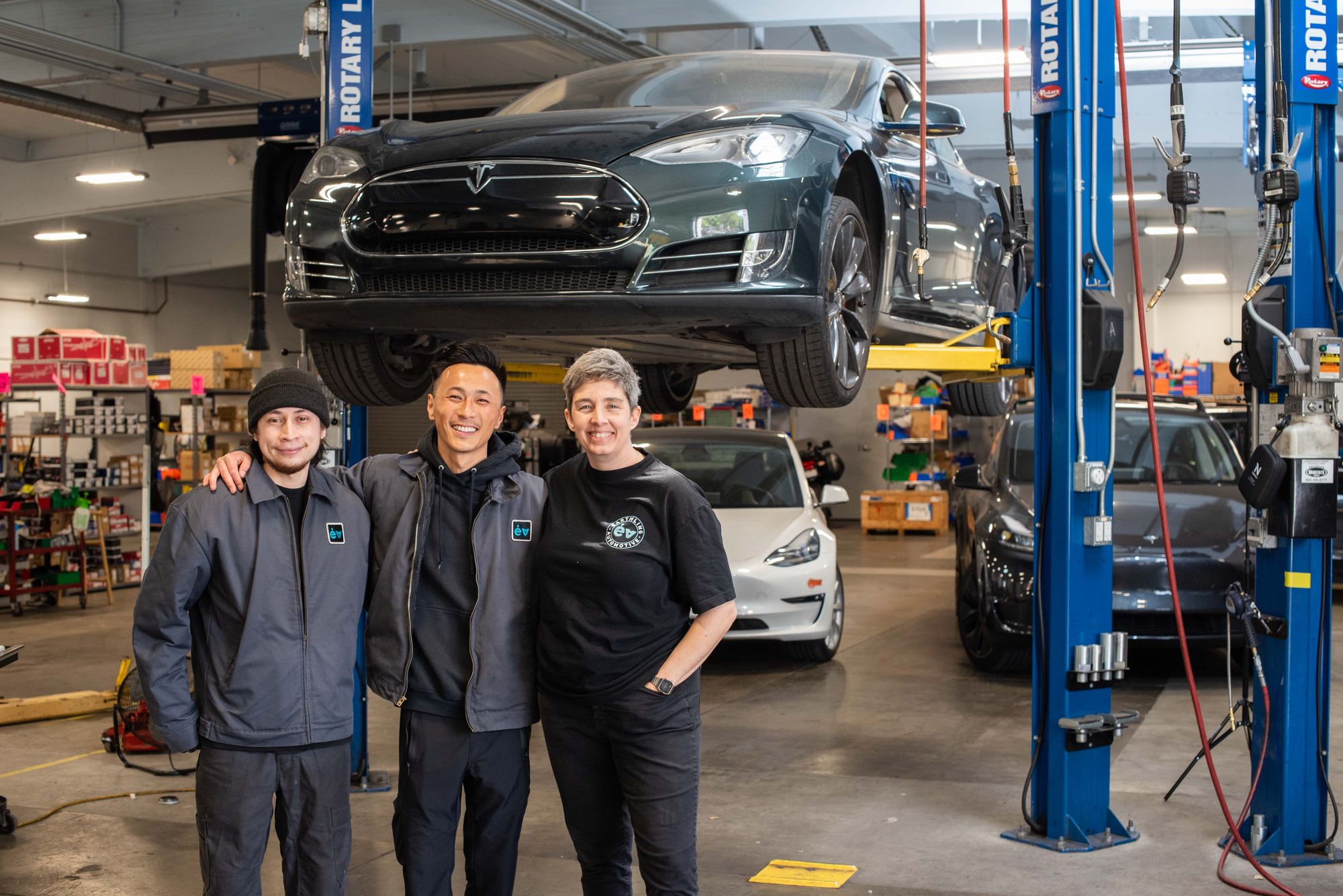 Three of the team under a Model S raised on a lift, with more Teslas behind them