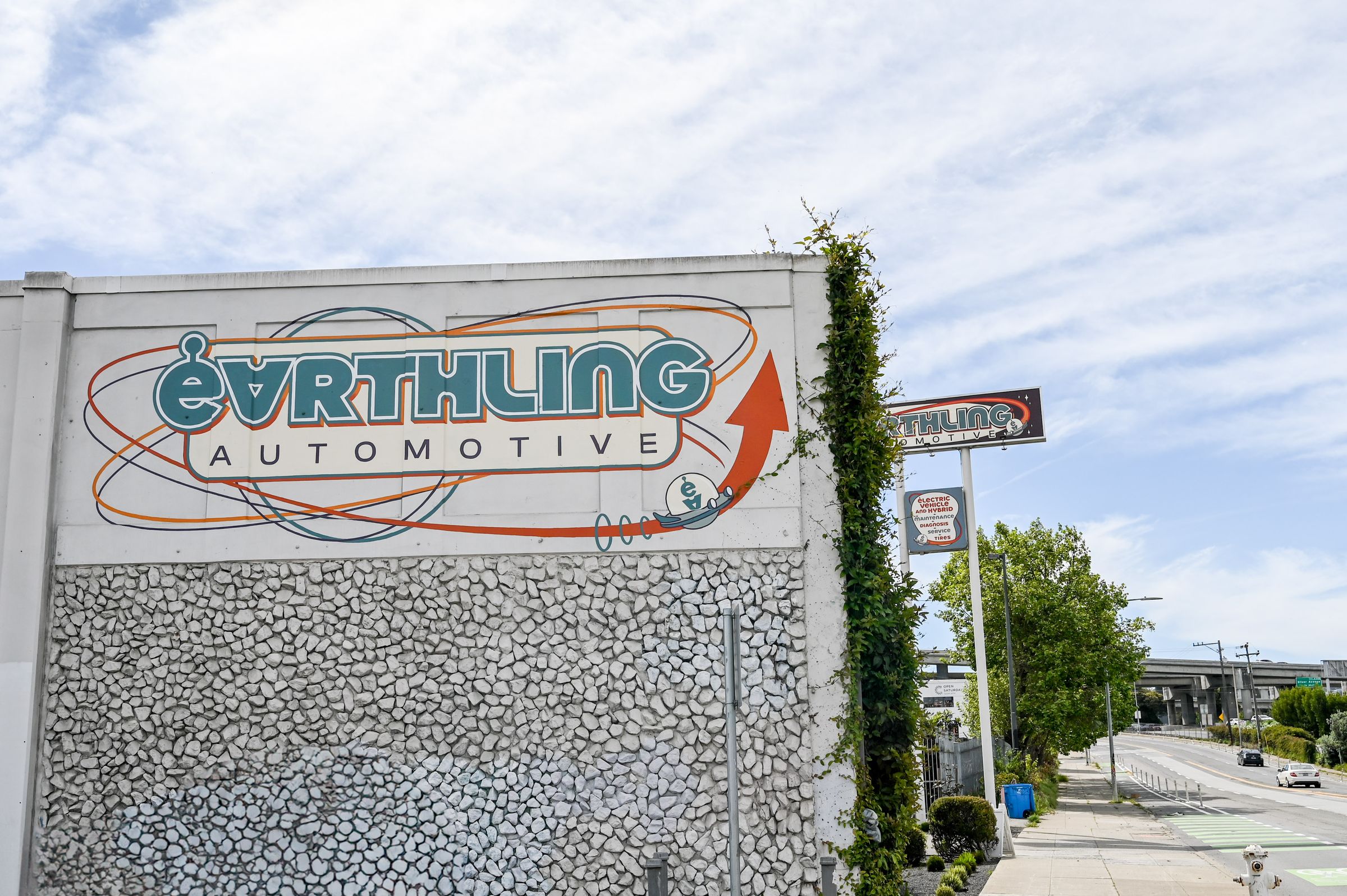 The Earthling Automotive sign painted on the shop's front wall on Bayshore Boulevard, under a blue sky